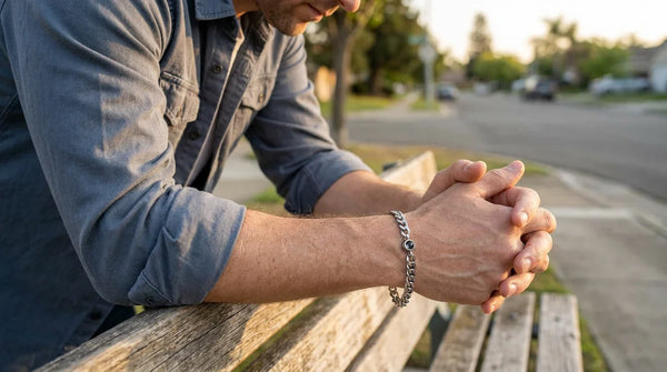 A father seated on a wooden bench at golden hour wearing a Brother & Sisters memorial photo bracelet