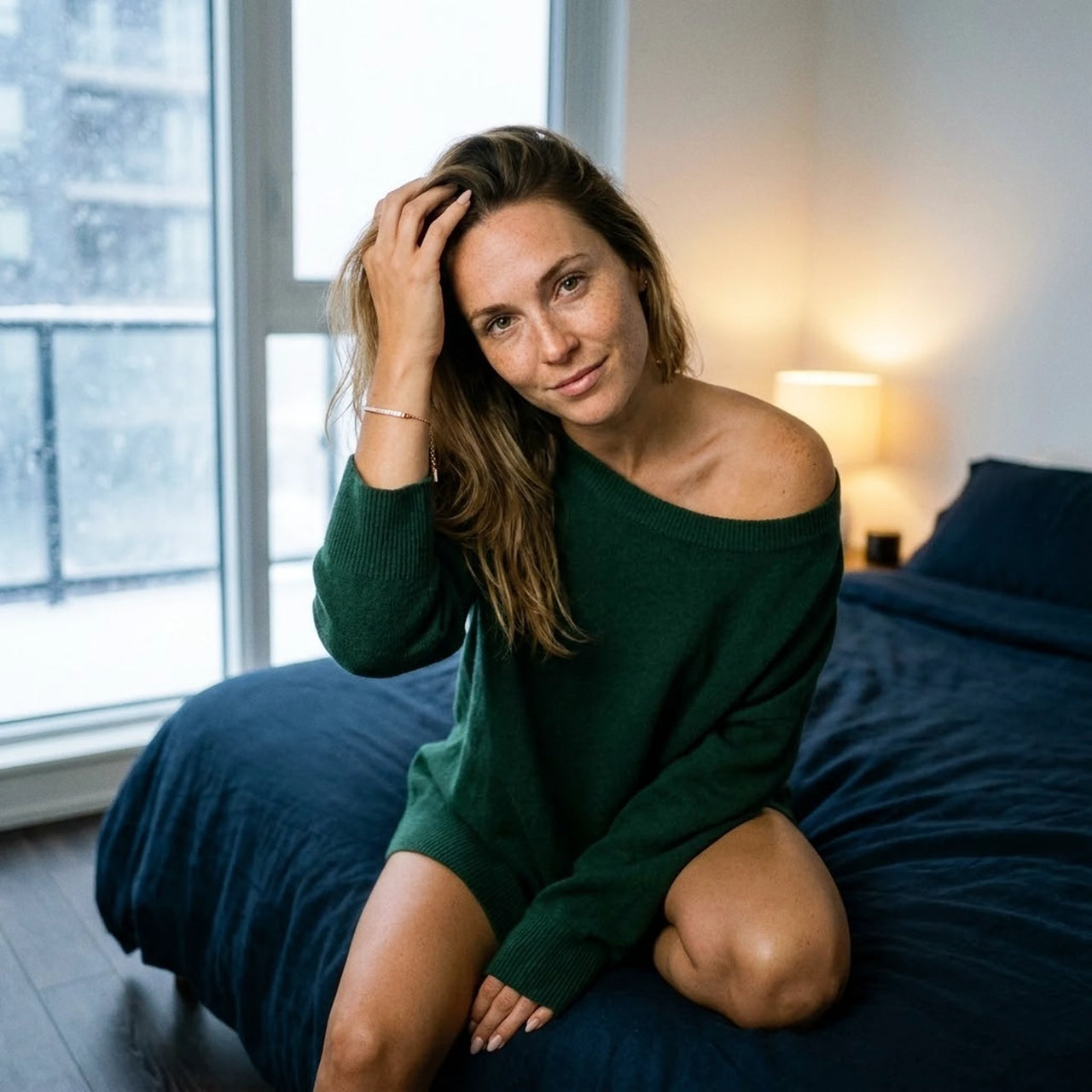 Woman in a green cashmere jumper wearing the rose gold Crystal Bar Bracelet, snow at the window