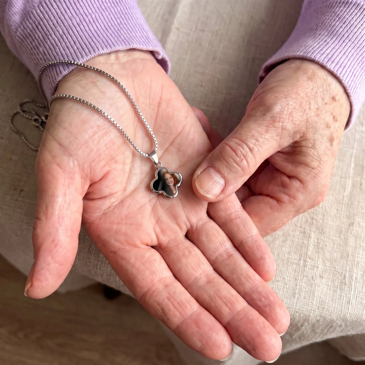 Thumb warming the silver clover pendant: the hidden photo appears under the thumb while the rest stays black | SKU: TPH-CLVN-SILVER