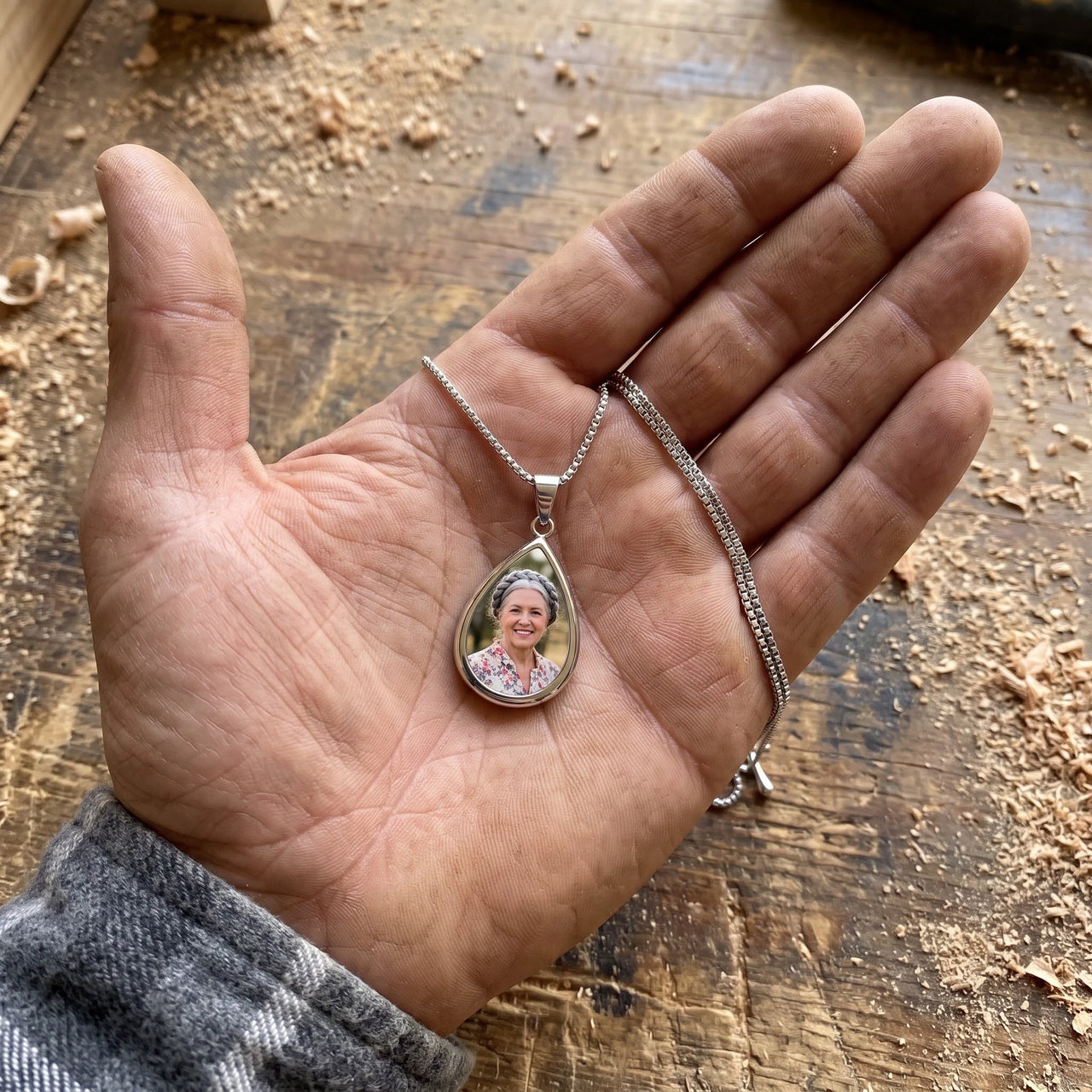 The silver teardrop photo pendant in a craftsman's open palm over a workbench, showing its real small size | SKU: TPH-DRPN-SILVER