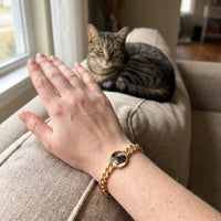 Thumbnail for Customer photo: the gold round bracelet with her cat's photo, her cat in the background | SKU: TPH-RNDB-GOLD